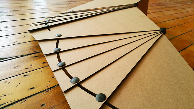 The rivets slide along channels cut into the cardboard, allowing the wings to expand and retract. 