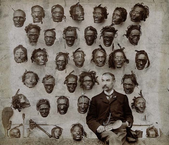 A man proudly sits with his severed head collection.