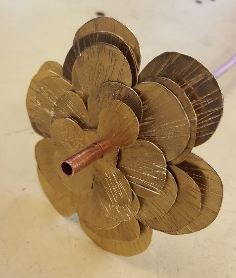 Time to assemble! He punched a quarter-inch hole through the center of all of the petals and then threaded them on a piece of copper tubing.