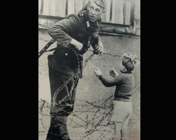 4.) A Berlin Wall Rescue: This German soldier from the East knew he shouldn’t let this child across the Berlin Wall, but he was separated from his parents. So, the guard lifts him across the barbed wire anyway, on the lookout for anyone who may catch him.